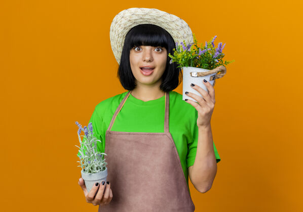 空间穿着制服的年轻女园丁兴奋地戴着园艺帽拿着花盆花盆橙色穿
