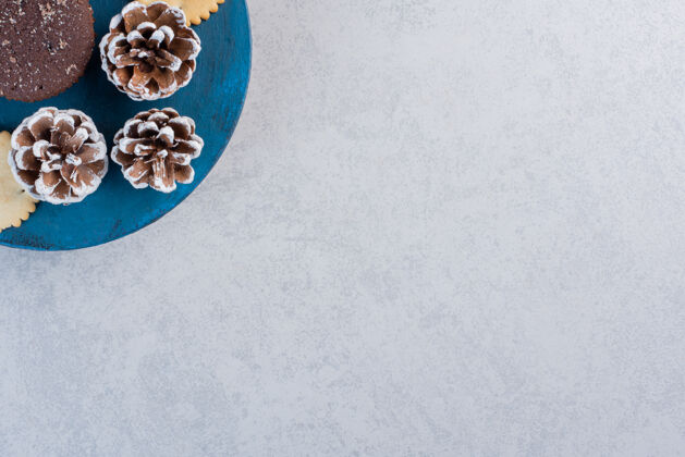 蛋糕饼干和巧克力蛋糕放在蓝色的木板上 松果放在大理石桌上复制空间烘焙食品美味