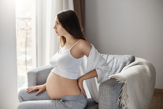 新年轻的孕妇按摩背部以减轻疼痛待在温暖舒适的家里室内休息为人父母