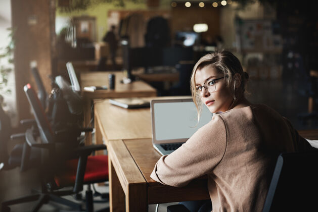 电话有魅力有决心的白人金发女人戴着眼镜 回头看镜头 坐在办公室里被同事打电话 通过笔记本电脑工作 与顾客交流咖啡馆专业人士信息