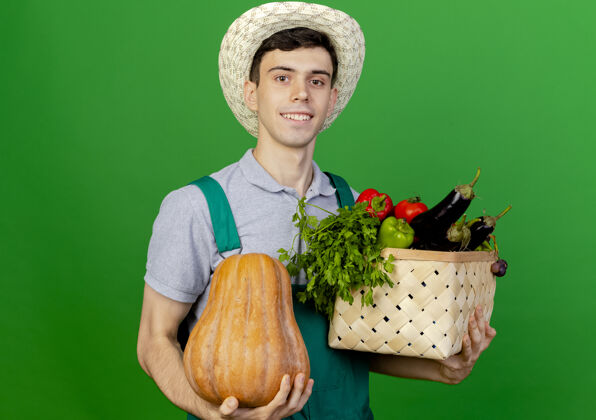 穿微笑的年轻男园丁戴着园艺帽 手里拿着南瓜和菜篮空间帽子持有