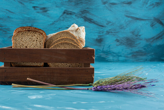 谷类食品一个木箱 里面装着蓝色背景的棕色新鲜面包片和小麦穗面包美味面包房