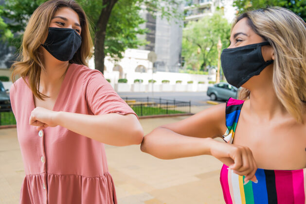 社会距离两个年轻朋友戴着口罩 肘部在户外颠簸的照片关怀病毒人
