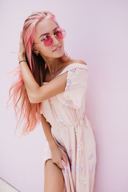 休闲可爱的白人女孩玩她的粉红色头发和微笑时尚的年轻女子在夏季礼服和太阳镜摆姿势欢呼粉色头发肖像