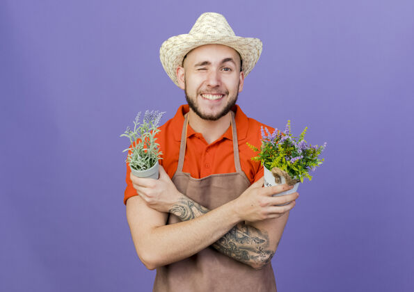 紫色微笑的男园丁戴着园艺帽 眨着眼睛 交叉双臂抱着花盆微笑交叉抱着