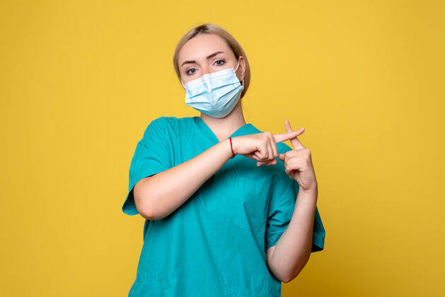 正面黄色墙壁上穿着医用衬衫和无菌口罩的年轻女医生的正面图成人护士肖像