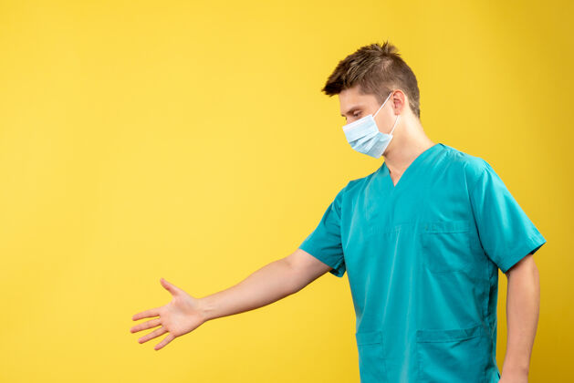 病毒身穿医疗服 戴着无菌口罩的男医生正对着黄色的墙上握手手面具人