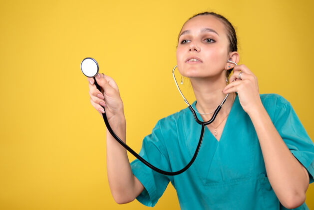 情绪黄色墙上穿着带听诊器的医用衬衫的女医生的正视图护士听诊器医生