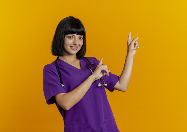 黑发微笑的年轻黑发女医生穿着制服用听诊器双手指向身后听诊器制服二
