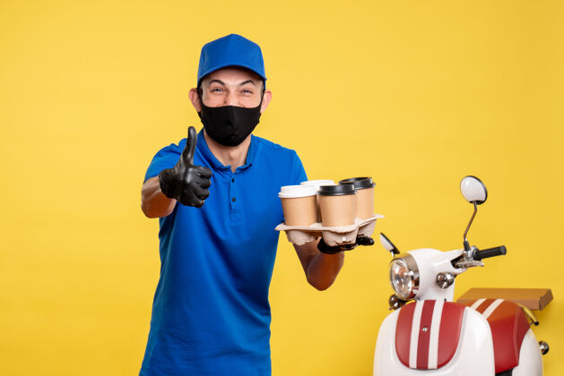 咖啡正面图：戴着黑色面具的男信使拿着咖啡 笑着穿上黄色的工作服前面视野大流行