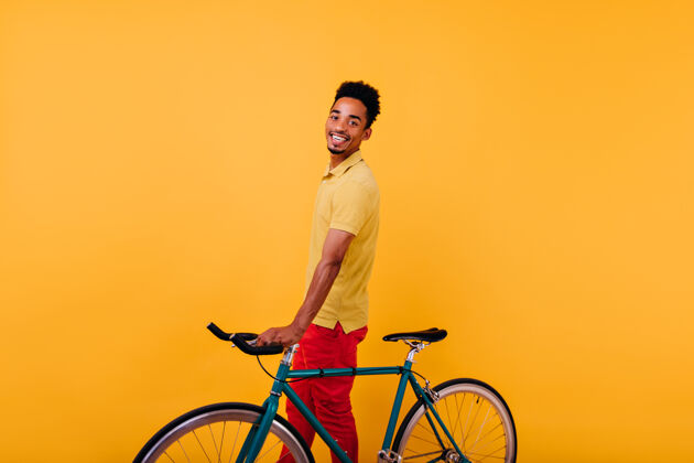 笑热情的黑人男子带着欢快的笑容和自行车合影室内照片是快乐的非洲男模和自行车站在一起表情微笑卷发