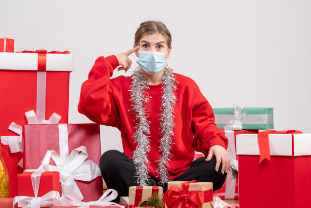 颜色正面图：年轻女性戴着无菌面具坐着 手里拿着圣诞礼物年轻女性绝育面具