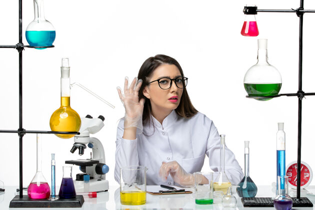 科学前视图穿着白色医疗服的女化学家正坐在白色背景的科学病毒冠状病毒-大流行实验室里拿着解决方案专业解决方案微笑