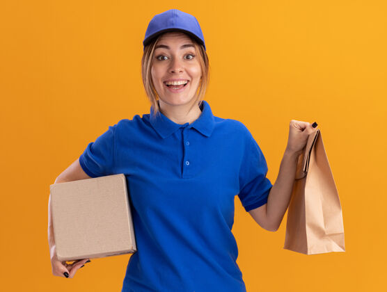 送货一个穿着制服的年轻漂亮的送货女孩拿着橙色的纸包和名片盒漂亮摆姿势惊喜