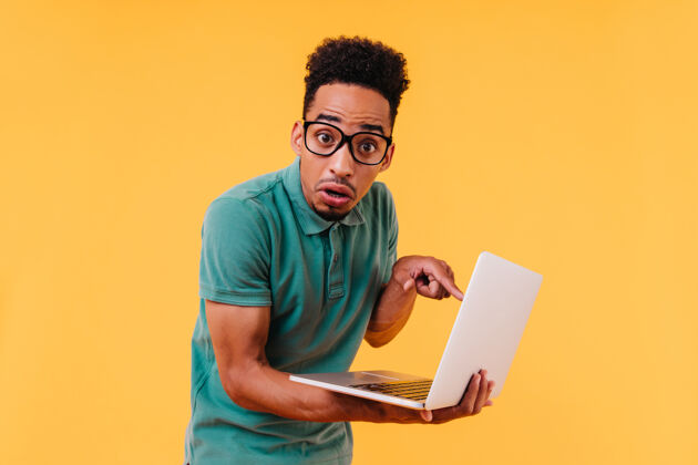 室内失望的非洲学生拿着笔记本电脑摆姿势震惊的黑人男性自由职业者拿着电脑教育大笑积极