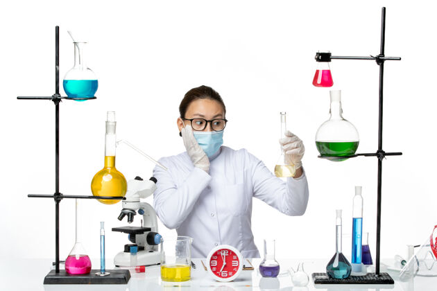 化学家前视图：穿着白色医疗服的女化学家 白色办公桌上戴着面罩 化学家实验室病毒冠状病毒飞溅瓶子病毒保持