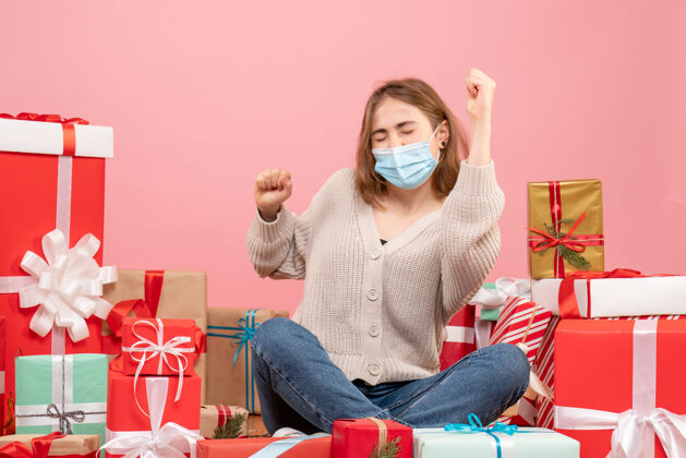 年份正面图：坐在圣诞节周围的年轻女性戴着无菌面具出现病毒礼物沙发