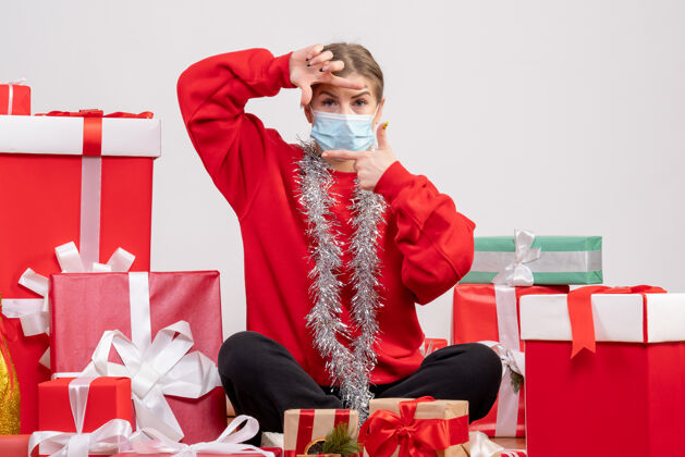 女士正面图：年轻女性戴着无菌面具坐着 手里拿着圣诞礼物病毒成人健康
