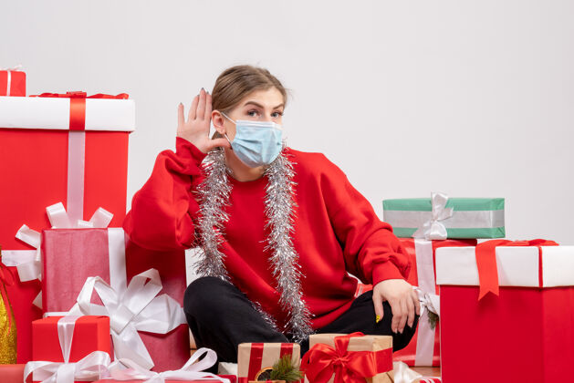 健康正面图：年轻女性戴着无菌面具坐着 手里拿着圣诞礼物坐着病毒情绪