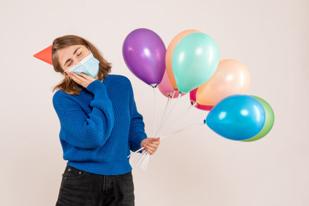 病毒正面图：戴着消毒面具的年轻女性手持五颜六色的气球年乐趣庆祝