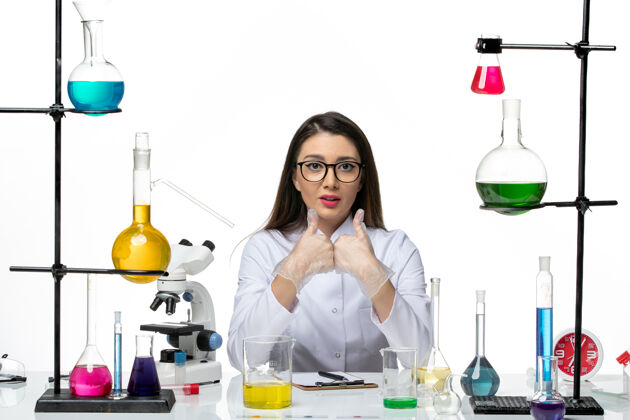 坐着前视图穿着白色医疗服的女化学家坐在白色背景上解决方案科学病毒冠状病毒-大流行实验室视图实验室烧杯