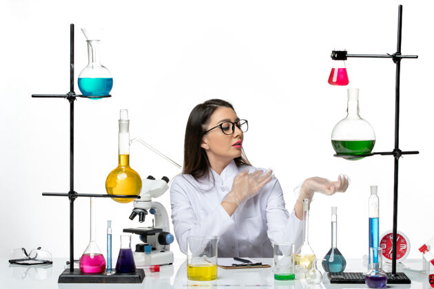 清洁前视图穿着白色医疗服的女化学家坐在白色背景的科学病毒冠状病毒-大流行实验室的解决方案大流行烧杯医学