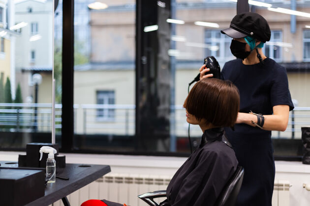理发师一个专业的女理发师给客户理发这个女孩戴着面具坐在美容院里客户时尚发廊