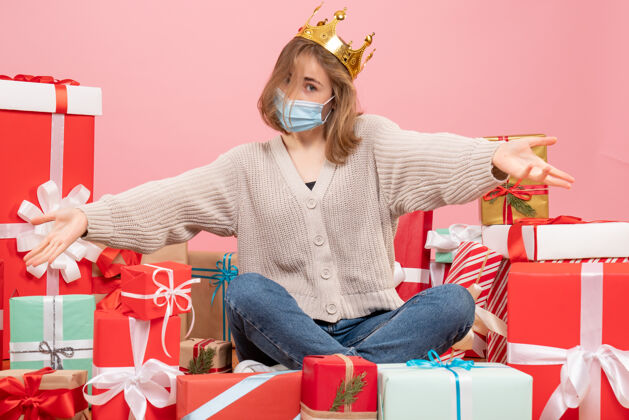 消毒正面图：坐在圣诞节周围的年轻女性戴着无菌面具出现成人粉色颜色