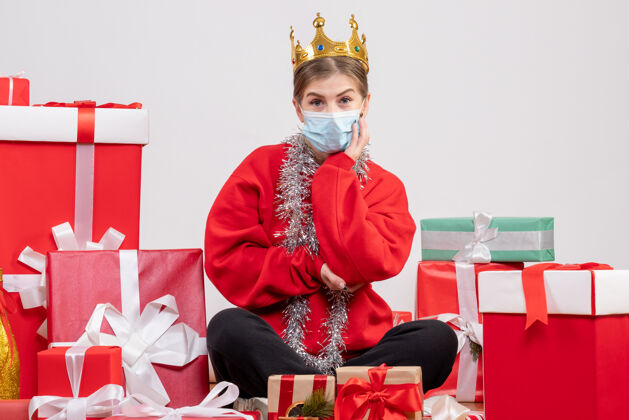 坐着正面图年轻女性戴着面具和皇冠坐在那里 手里拿着圣诞礼物年轻女性礼物皇冠