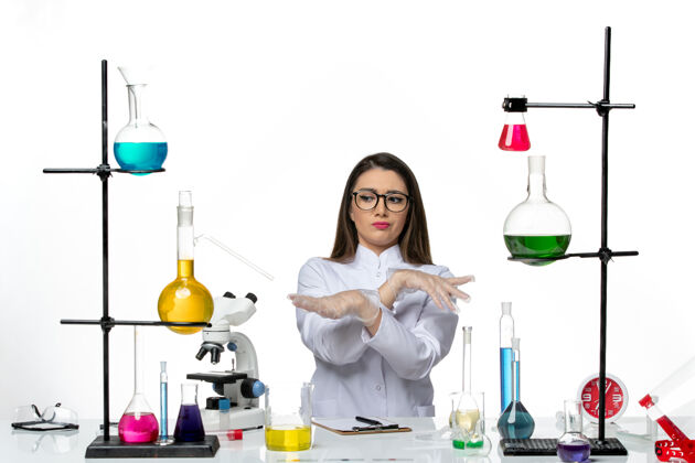 容器前视图穿着白色医疗服的女化学家坐在浅白背景上实验室病毒冠状病毒大流行科学葡萄酒前面病毒