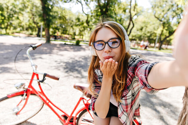 快乐迷人的戴着眼镜的女孩在红色自行车前自拍夏日早晨愉快的欧洲女士在公园休息的户外照片活动美丽城市