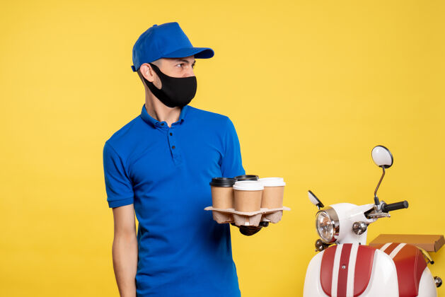 面具正面图身穿蓝色制服 戴着面具的男信使拿着咖啡 穿着黄色制服 工作服 工作大流行咖啡修理工视图