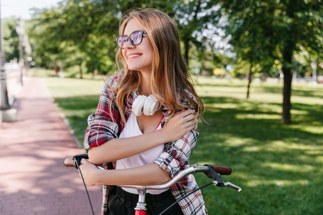 放松梦幻般的白人女孩骑着自行车微笑着环顾四周戴着眼镜的漂亮小姐站在公园里自然成人女人
