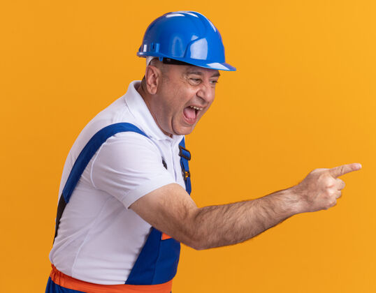 人恼怒的白人成年建筑工人穿制服 看了看 并指出在橙色的一边侧线人制服