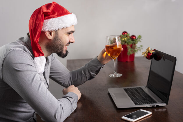欢乐特写镜头一个西班牙裔男子戴着圣诞老人的帽子 享受他的酒 有和网上会议西班牙裔聚会帽子