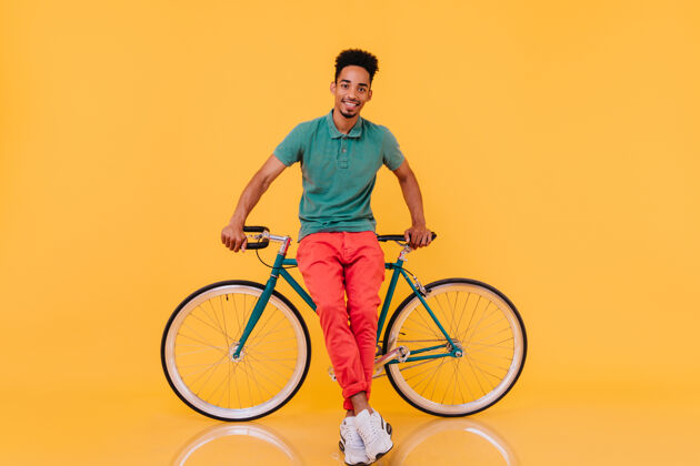自行车微笑优雅的黑发男子在自行车旁愉快地摆出姿势热情的非洲男子骑着绿色自行车的室内肖像家伙冷静年轻