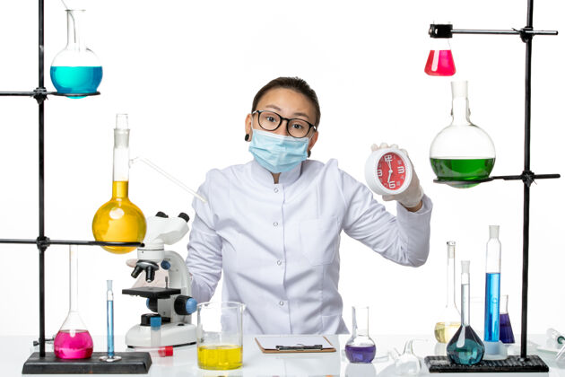 科学前视图穿着医疗服的女化学家 戴着面具 白色背景上拿着红色的时钟病毒实验室化学冠状病毒-飞溅面具实验室医生