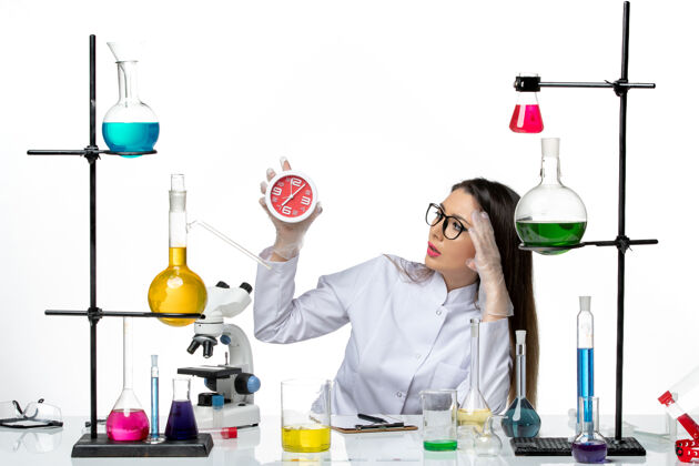 工作前视图穿着白色医疗服的女化学家拿着白色背景上的时钟科学病毒实验室柯维德大流行前面医生实验室