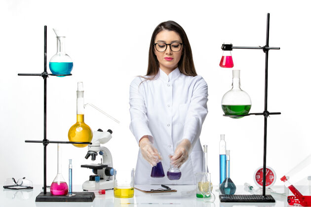 病毒正面图：穿着无菌医疗服的女化学家拿着装有紫色溶液的烧瓶 背景是白色的病毒疾病冠状病毒-大流行科学实验室视图科学