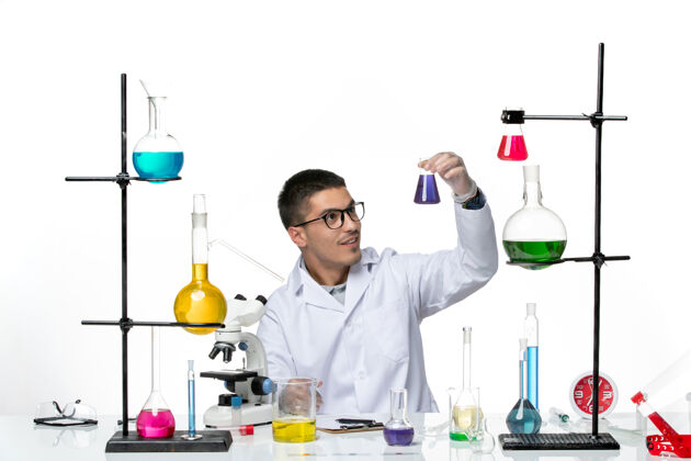 实验室正面图身着医疗服的男性化学家坐着拿着白色背景上紫色溶液的烧瓶病毒冠状病毒飞溅疾病科学坐医学西装