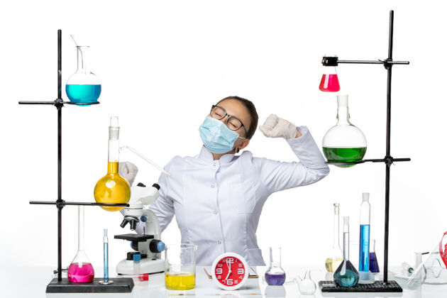 哈欠前视图：穿着医疗服的女化学家 戴着面罩 坐在溶液里 打着哈欠 背景是白色的病毒 实验室里的化学成分是covid飞溅物前面医生实验室