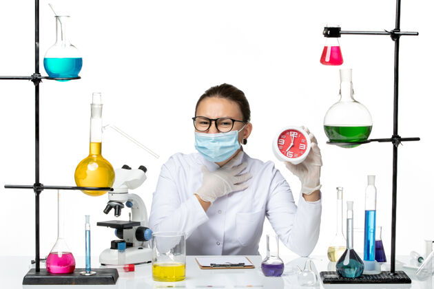 视图前视图穿着医疗服的女化学家 戴着面具 白色背景上拿着红色的时钟病毒化学冠状病毒-飞溅实验室实验室西装时钟