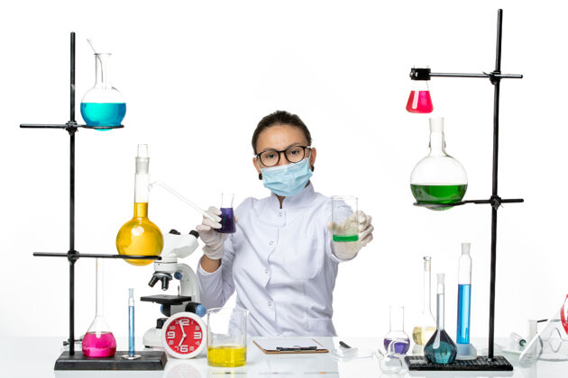 视图前视图穿着医疗服的女化学家 戴着面罩 在浅白色背景上拿着不同的溶液 飞溅着病毒化学实验室的病毒实验室医生持有