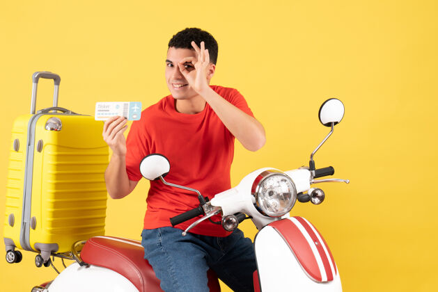 球员正面图骑着轻便摩托车的快乐的年轻人拿着车票 把奥基标志放在他的标志前面举行车辆视图