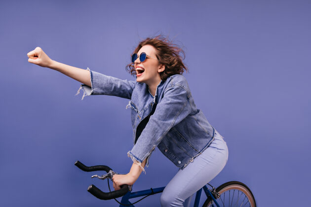 快乐坐在自行车上 挥手微笑的时髦女士可爱的白人女自行车手的肖像放松紫色休闲