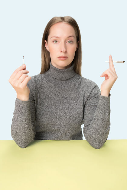 女性坐在画室桌子旁抽烟的年轻女子流行的颜色极简风格的白种女孩肖像 带复印空间烟草侧面孤独