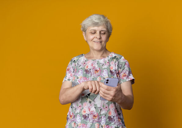 请拿着高兴的老妇人抱着电话 看着隔离在橙色墙上的电话橙色老人电话