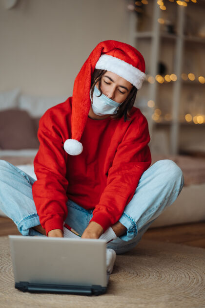 年轻在笔记本电脑旁戴着圣诞帽的家伙正在通过视频通话进行互动在家里过圣诞节是一种与世隔绝的生活在假期里是一种社交距离欢呼电脑语言