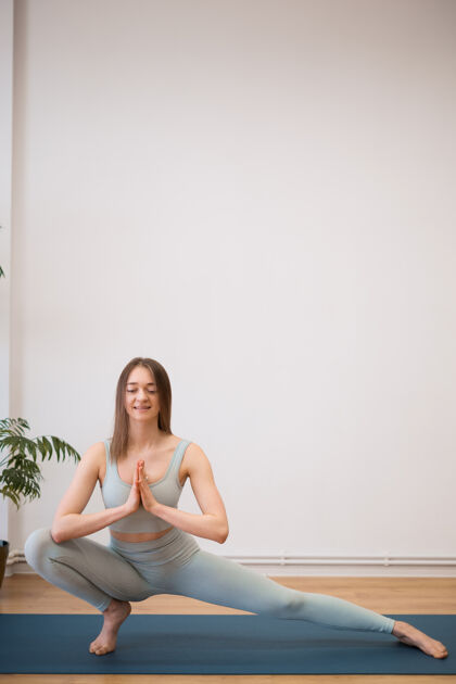 专注运动型年轻女子在白色墙壁上用植物练习瑜伽-健活的概念 身体和心理发展之间的自然平衡禅宗灵活训练