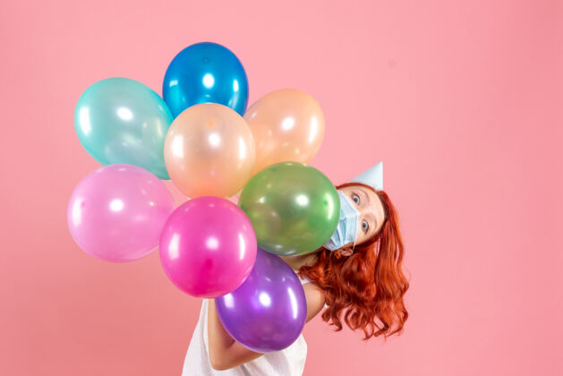 聚会正面图年轻的女性手持彩色气球在面具上浅粉色颜色气球乐趣